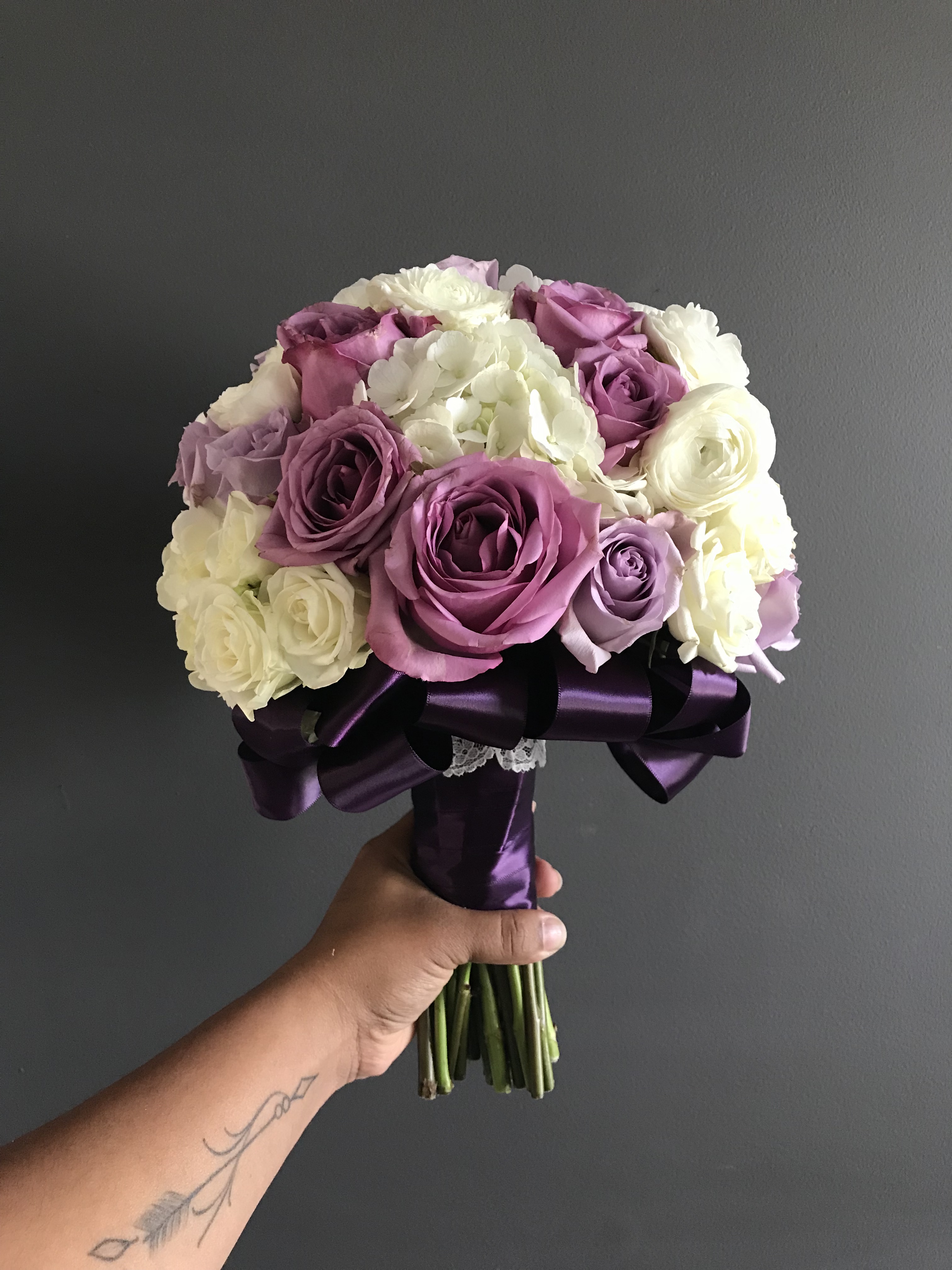 Bridal bouquet with lavender roses, white hydrangea, white ranunculus and white spray roses embellished with purple satin ribbon