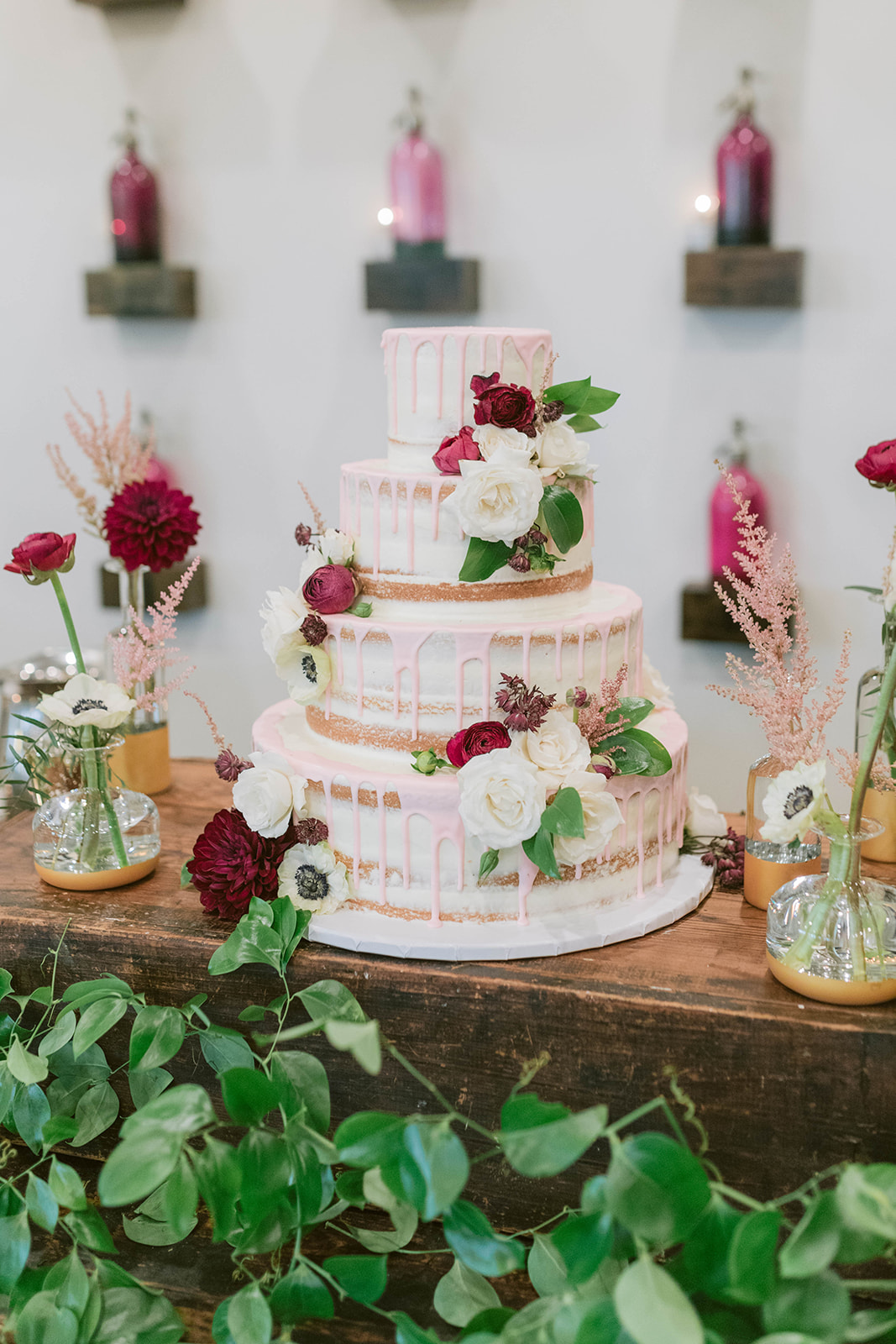 naked drip cake in blush adorned with burgundy and ivory flowers