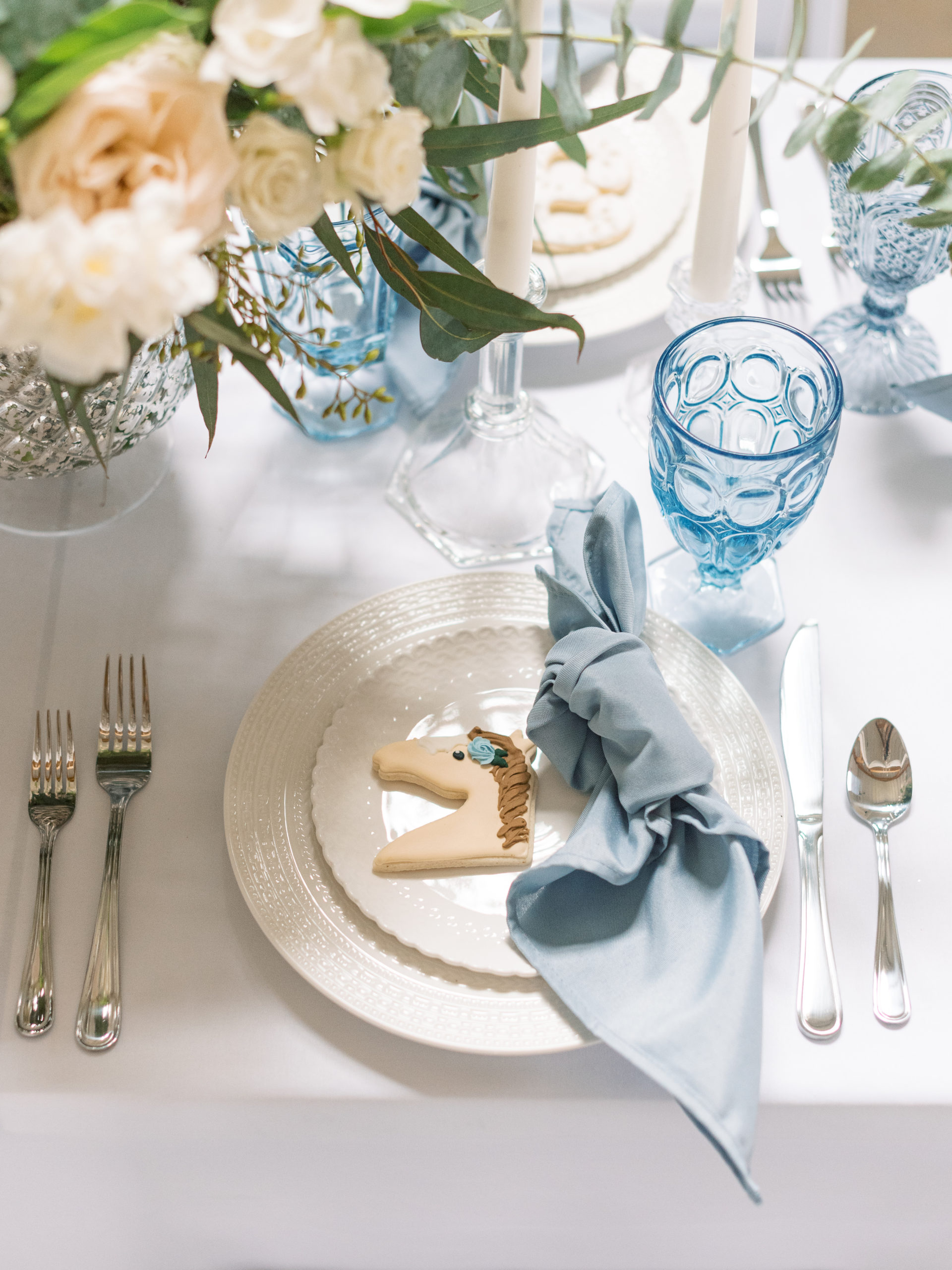  beautiful white plates, blue napkins, blue goblets and a cute horse cookie